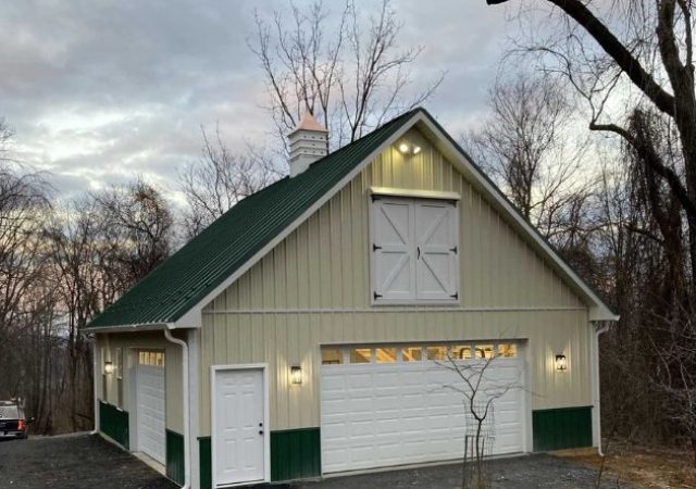 detached garage with cream metal siding, white garage door, and gray metal roofing