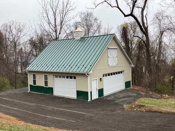 detached garage with green metal roofing, white metal siding, and two white garage doors
